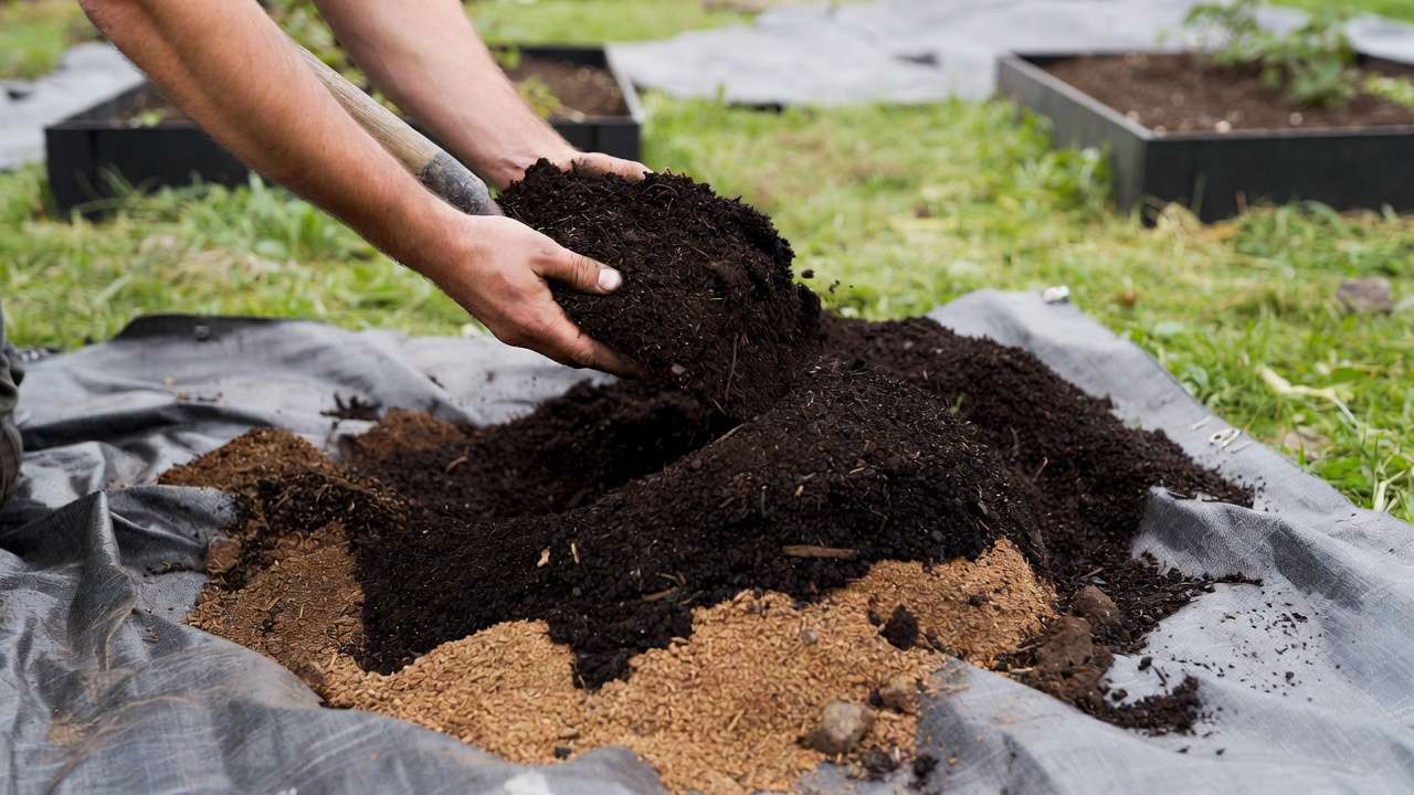 Hands-on mixing of raised bed soil recipe with topsoil and compost in a garden setting.